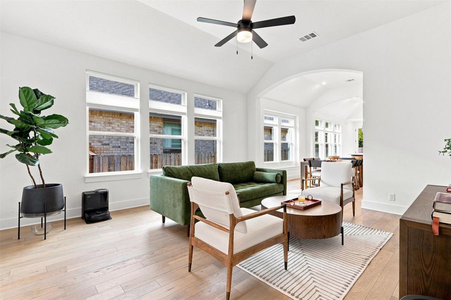 Sunlight streams through large windows onto hardwood flooring under a high vaulted ceiling.