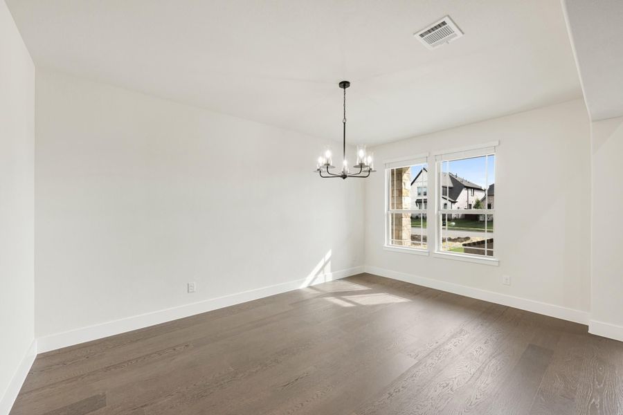 Empty dining room with dark hardwood floors, white walls, chandelier, and double window