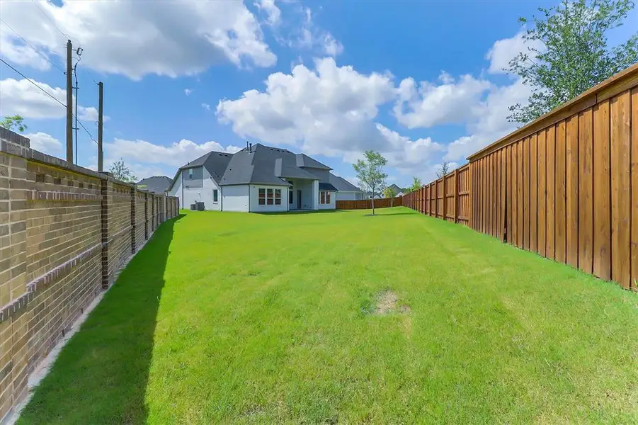 Expansive backyard featuring a lush green lawn, a tall wooden privacy fence, and a brick perimeter wall Expansive backyard featuring a lush green lawn, a tall wooden privacy fence, and a brick perimeter wall