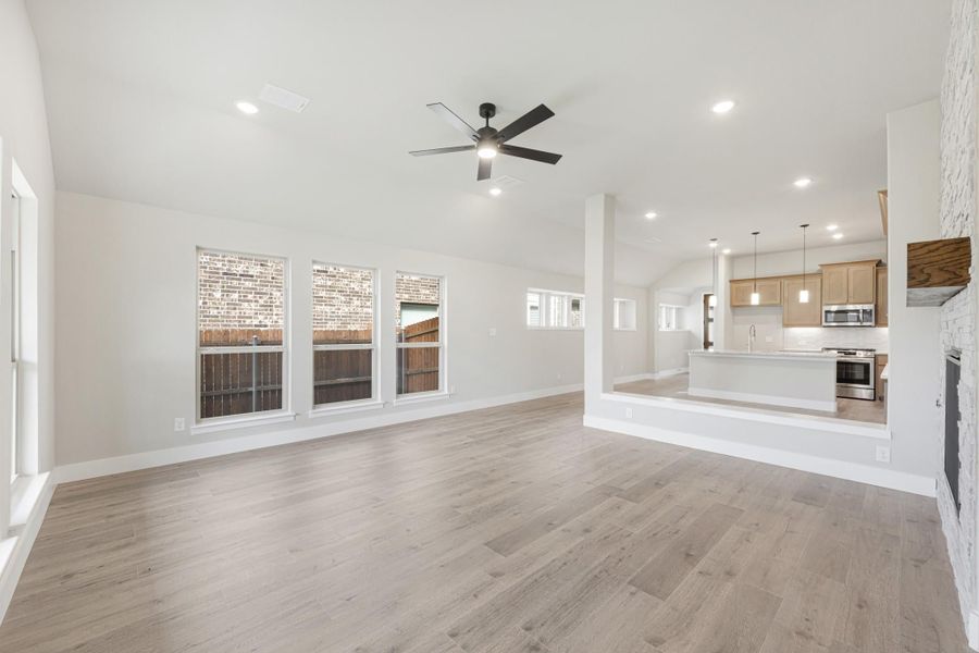 Open living room with hardwood floors and ceiling fan, open to kitchen with island and stainless appliances