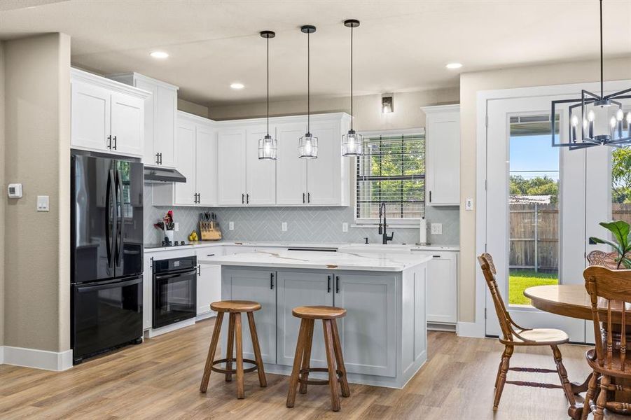 Kitchen featuring white shaker cabinetry, an island with light blue lower cabinetry, wood-finish flooring, a herringbone tile backsplash, and stainless steel appliances
