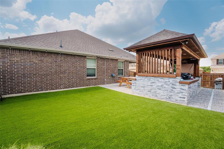 Back of property featuring roof with shingles, a patio, brick siding, and exterior kitchen Back of property featuring roof with shingles, a patio, brick siding, and exterior kitchen