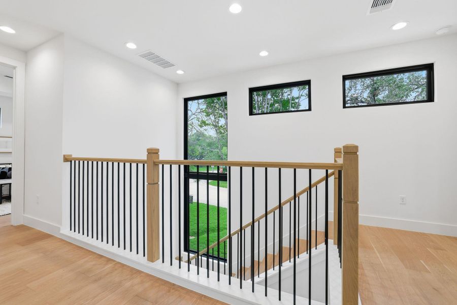 Modern upper landing featuring light wood-finish flooring and a contemporary staircase with black metal balusters and a wood handrail