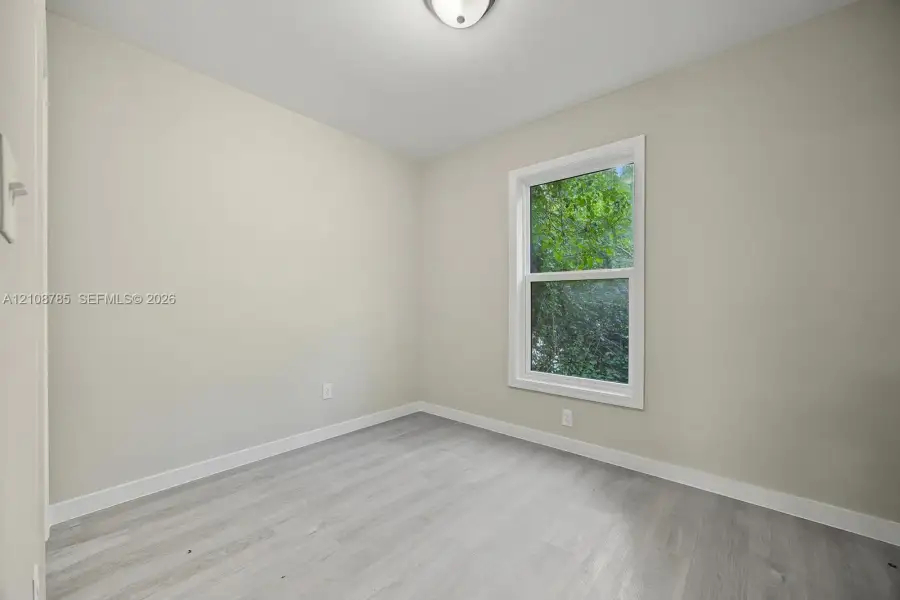 Neutral-toned walls, wood-finish flooring, and a double-hung window with a verdant exterior outlook, illuminated by a ceiling-mounted light fixture Neutral-toned walls, wood-finish flooring, and a double-hung window with a verdant exterior outlook, illuminated by a ceiling-mounted light fixture