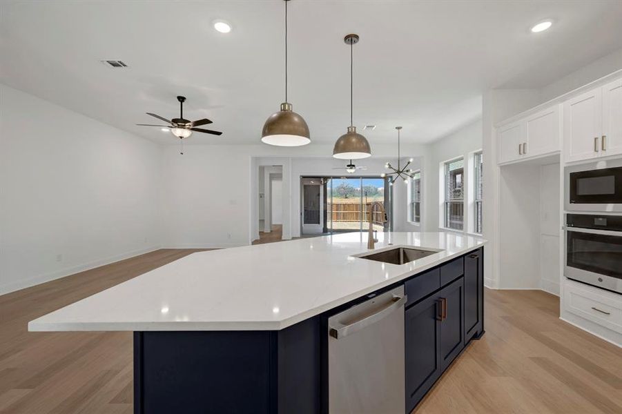 Two tone kitchen featuring dual tone cabinets, stainless steel appliances, a center island with sink, open floor plan, and light stone counters