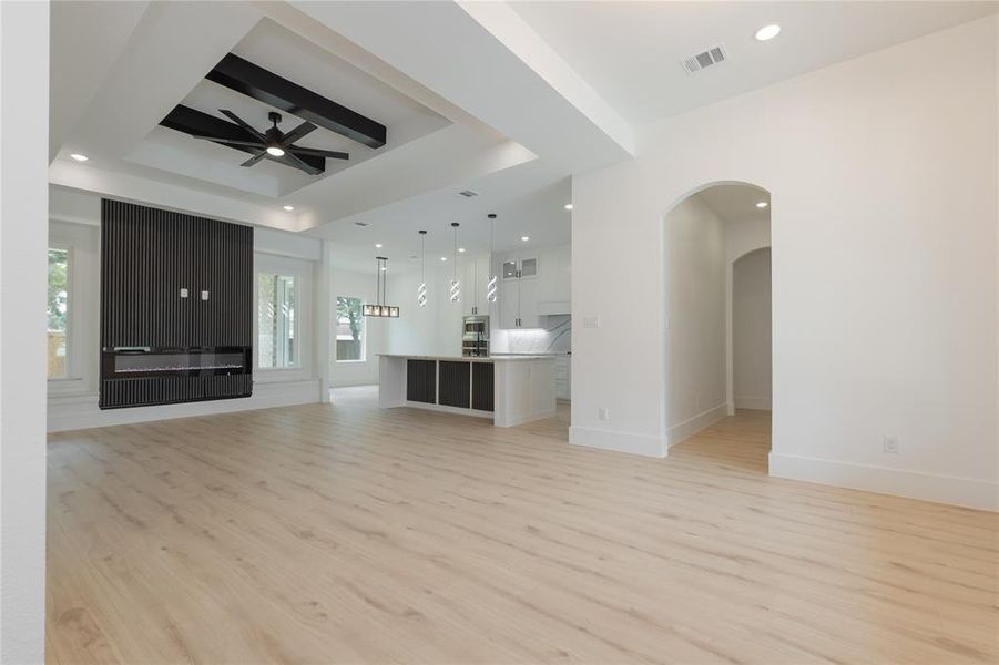 Unfurnished living room with light wood-type flooring, a ceiling fan, recessed lighting, and a raised ceiling