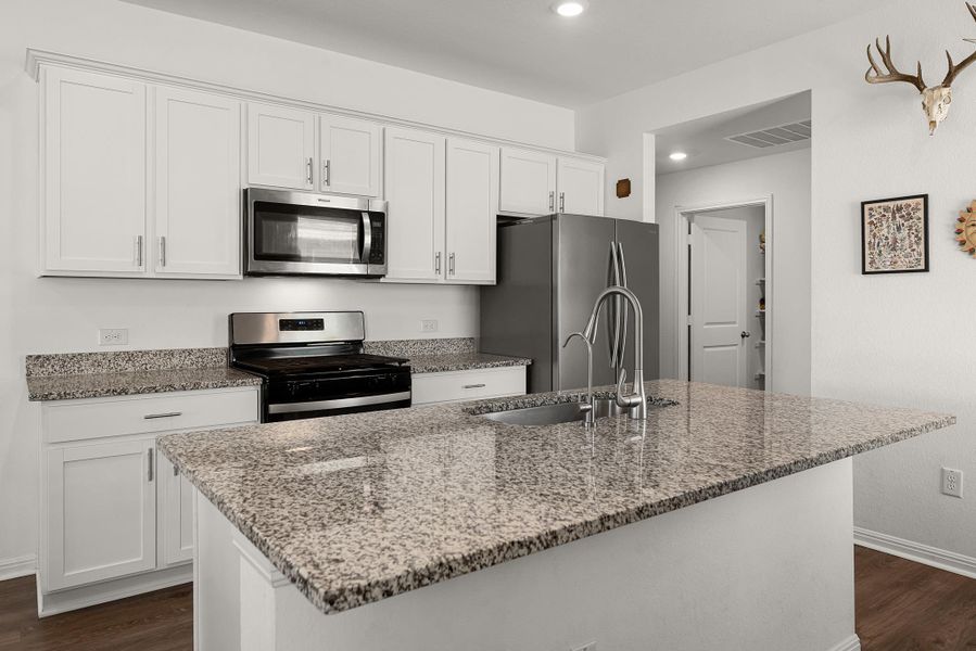 Kitchen with stainless steel appliances, light stone counters, dark wood finished floors, white cabinets, and a kitchen island with sink