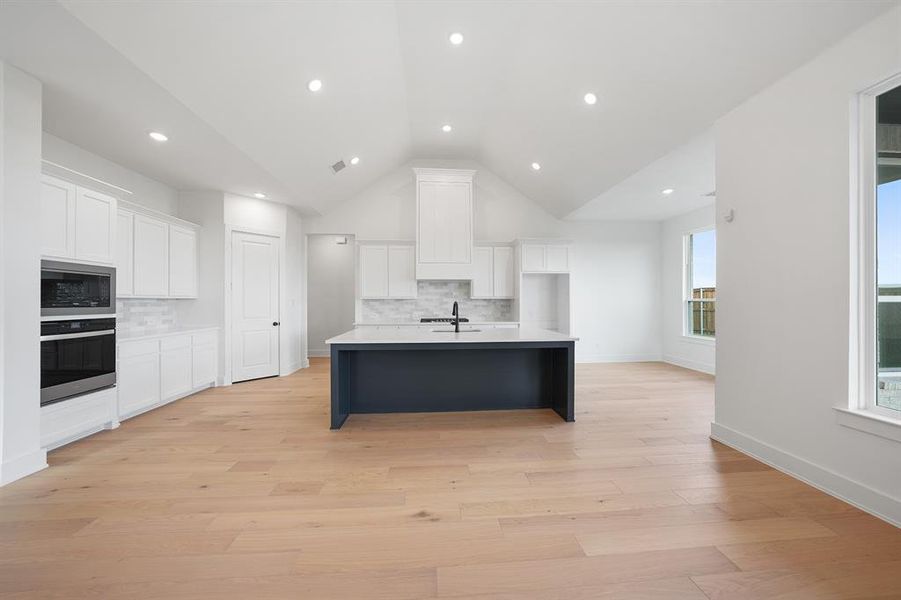 Kitchen with white cabinets, stainless steel appliances, lofted ceiling, light wood-style flooring, and recessed lighting