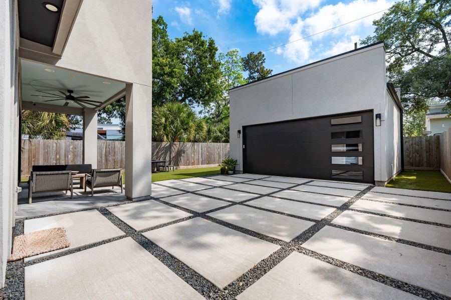 The detached two-car garage features modern sconces on each side, epoxy flooring, and a sleek concrete paver driveway with rock inlay detail for added curb appeal.