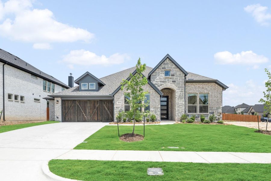 Single-story home with stone and brick exterior, wood garage doors, arched entry, and green front lawn Single-story home with stone and brick exterior, wood garage doors, arched entry, and green front lawn