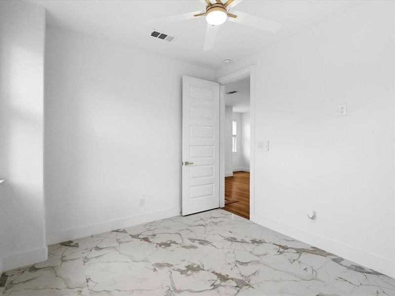 Room featuring marble-look tile flooring, white walls, and a white ceiling fan with gold-tone accents