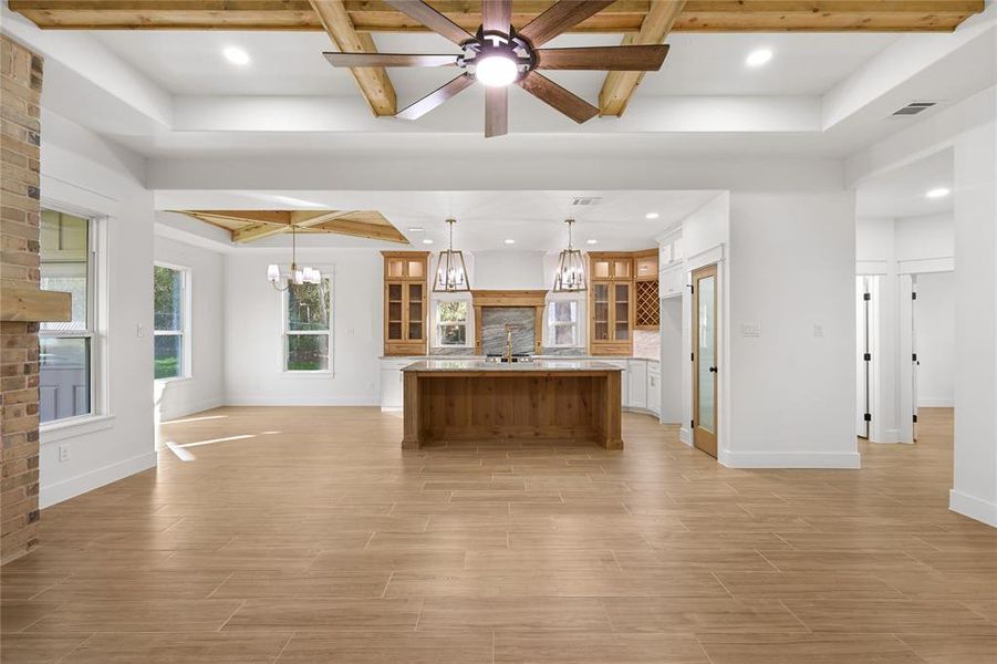 Kitchen featuring open floor plan, beam ceiling, glass insert cabinets, a kitchen island with sink, and brown cabinets