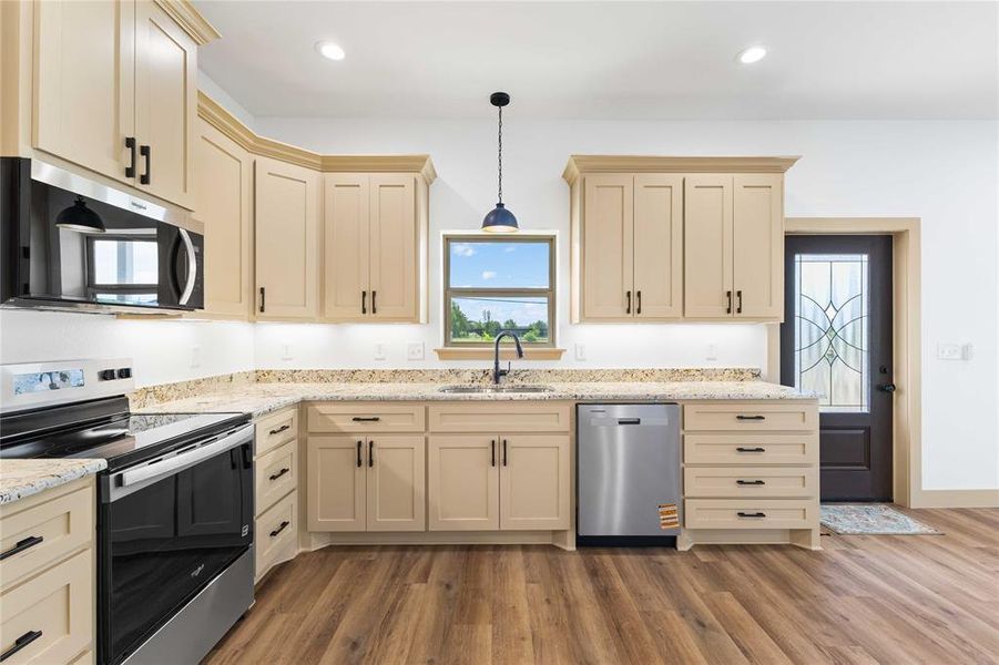 Kitchen featuring cream cabinetry, appliances with stainless steel finishes, light stone countertops, hanging light fixtures, and light wood-style floors