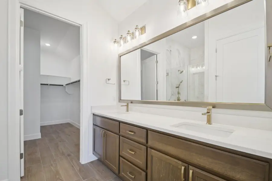 Full bathroom with a marble finish shower, double vanity, a spacious closet, wood finish floors, and recessed lighting