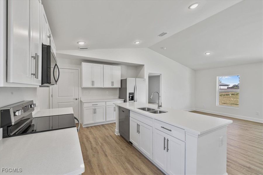 Kitchen with appliances with stainless steel finishes, white cabinetry, light wood-style flooring, lofted ceiling, and a center island with sink
