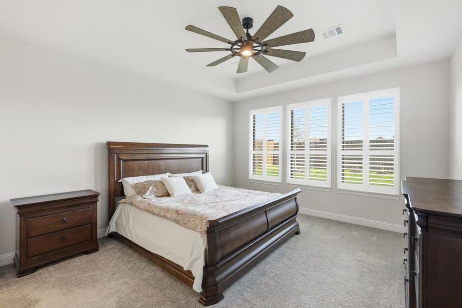 Bedroom featuring a raised ceiling, light carpet, and ceiling fan