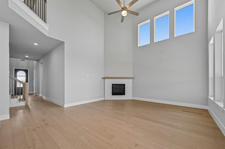 Unfurnished living room featuring a towering ceiling, a glass covered fireplace, light wood-type flooring, stairway, and ceiling fan