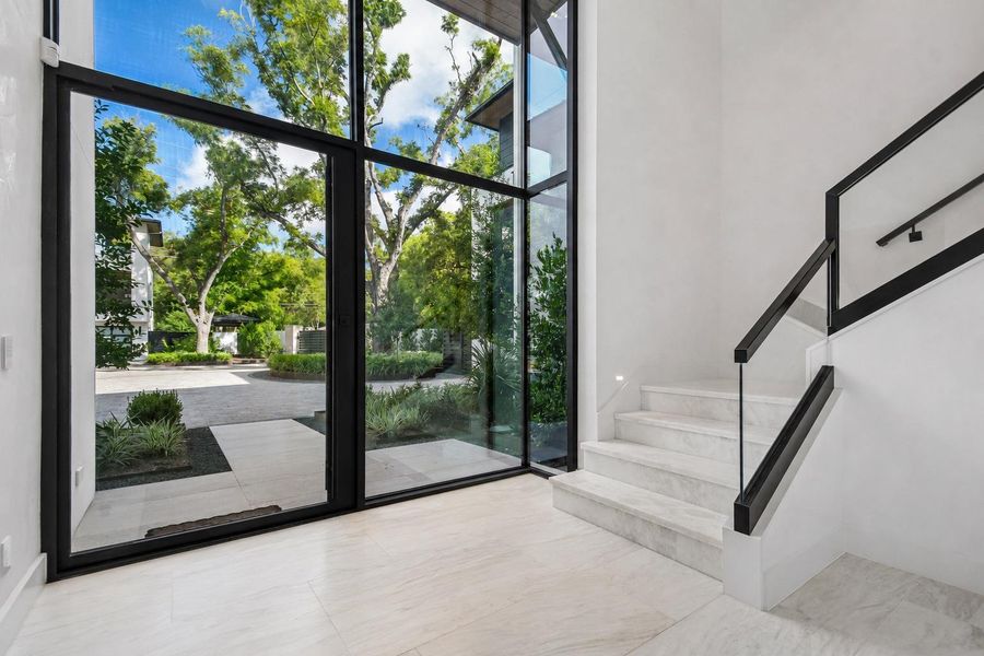 Floor-to-ceiling glass walls frame serene outdoor views in this modern entryway with marble flooring. Floor-to-ceiling glass walls frame serene outdoor views in this modern entryway with marble flooring.