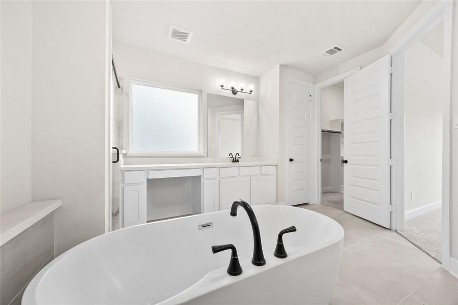 The primary bathroom features a freestanding bathtub with sleek black fixtures. It has a spacious vanity area with ample storage and a large mirror. The room is bright, with natural light from a frosted window. The primary bathroom features a freestanding bathtub with sleek black fixtures. It has a spacious vanity area with ample storage and a large mirror. The room is bright, with natural light from a frosted window.