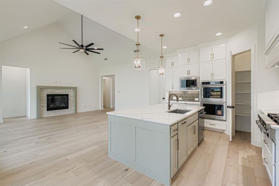 Kitchen featuring hanging light fixtures, high vaulted ceiling, light wood-style flooring, open floor plan, and ceiling fan Kitchen featuring hanging light fixtures, high vaulted ceiling, light wood-style flooring, open floor plan, and ceiling fan