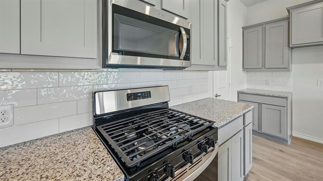 Kitchen featuring appliances with stainless steel finishes, light stone countertops, backsplash, gray cabinets, and light wood-type flooring