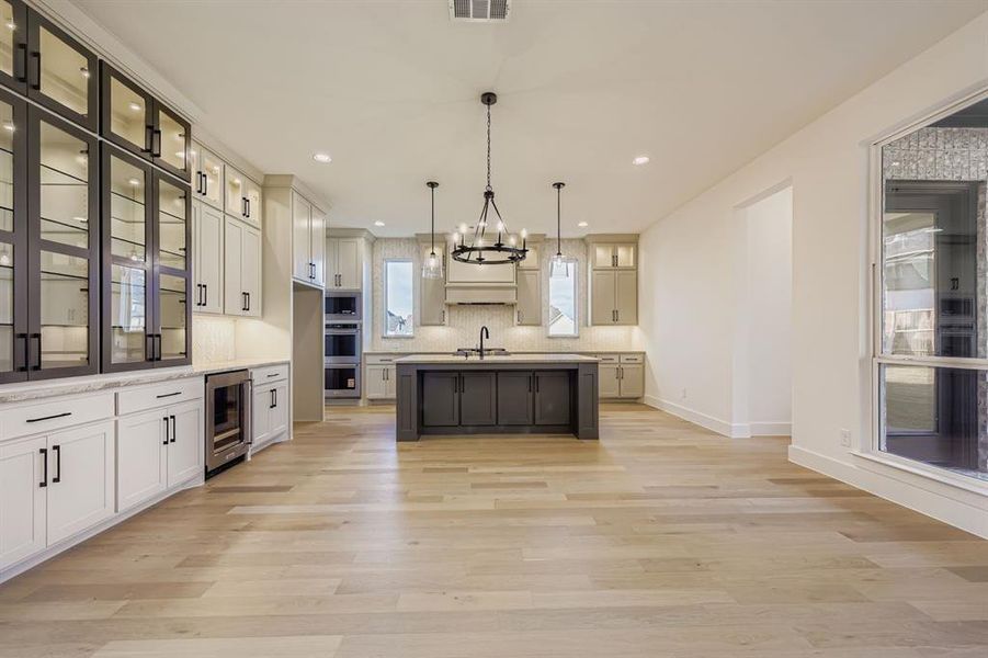 Kitchen featuring glass insert cabinets, pendant lighting, white cabinets, a chandelier, and a kitchen island with sink