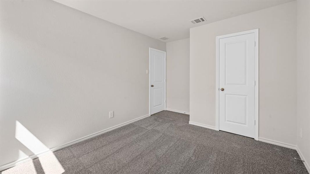 Neutral-toned walls complement the gray carpeting in this room, featuring two white two-panel doors with round knobs and white baseboards