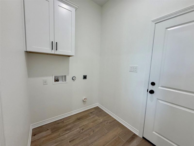 Utility room featuring wood-finish flooring, white cabinetry with matte black hardware, and a white paneled door