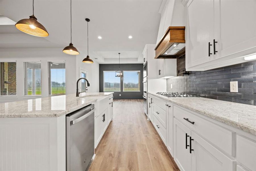 Kitchen with a kitchen island with sink, appliances with stainless steel finishes, white cabinets, and decorative light fixtures