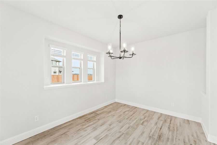 Empty dining room with light wood floors, white walls, black chandelier, and triple windows Empty dining room with light wood floors, white walls, black chandelier, and triple windows