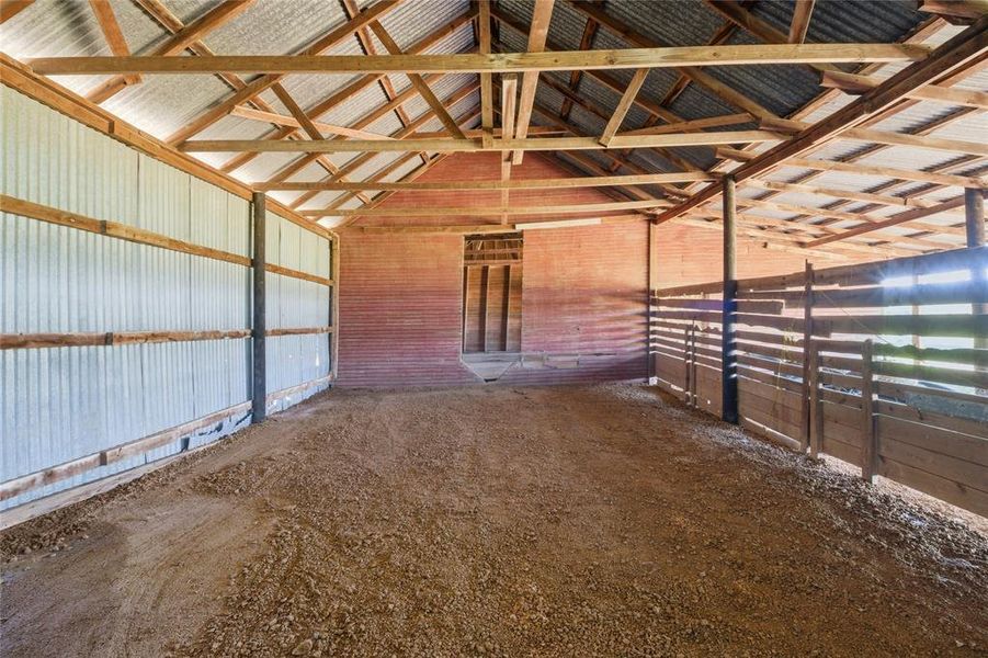 Spacious barn interior featuring exposed wooden rafters, a corrugated metal roof, brick walls, corrugated metal siding, and a dirt floor