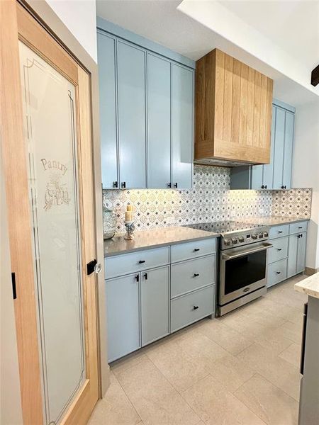 Kitchen featuring decorative backsplash, stainless steel range with electric stovetop, light tile patterned floors, and premium range hood