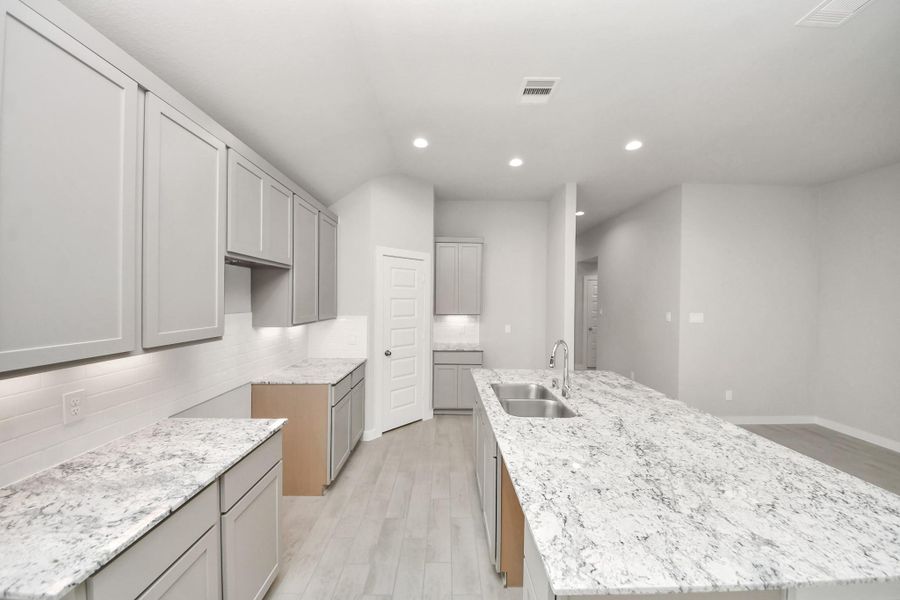 The kitchen is a culinary haven, featuring granite countertops, a tile backsplash, stainless steel appliances, 42” upper cabinets, and undercabinet lighting. Sample photo of completed home with similar floor plan. Actual colors and selections may vary. The kitchen is a culinary haven, featuring granite countertops, a tile backsplash, stainless steel appliances, 42” upper cabinets, and undercabinet lighting. Sample photo of completed home with similar floor plan. Actual colors and selections may vary.