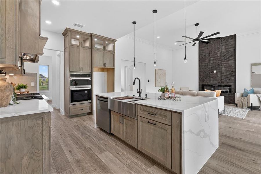 Kitchen featuring light stone countertops, open floor plan, a tiled fireplace, a kitchen island with sink, and light wood-type flooring