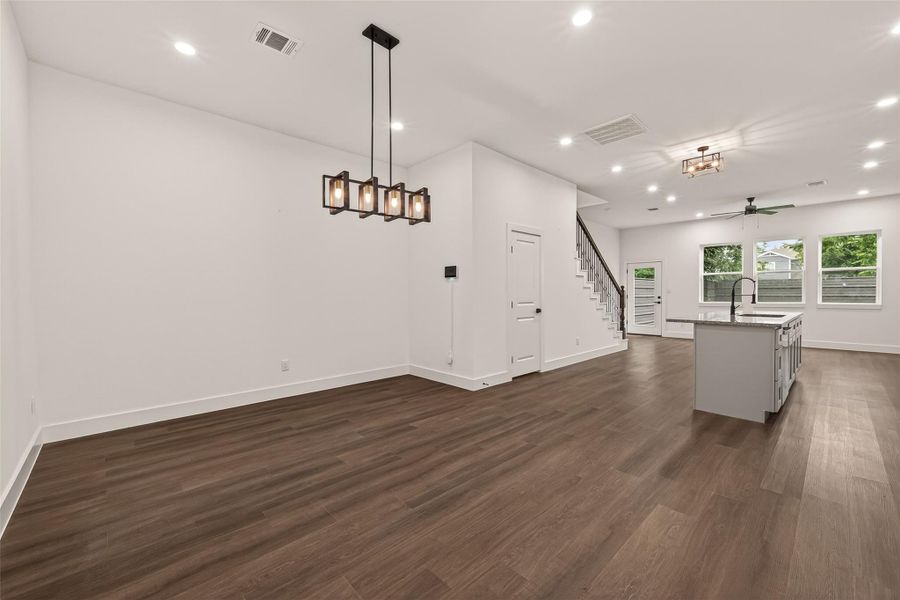 This open-concept living space features elegant engineer wood flooring, modern light fixtures, and a sleek kitchen island. The area is well-lit with recessed lighting and large windows, and there's easy access to the staircase. This open-concept living space features elegant engineer wood flooring, modern light fixtures, and a sleek kitchen island. The area is well-lit with recessed lighting and large windows, and there's easy access to the staircase.