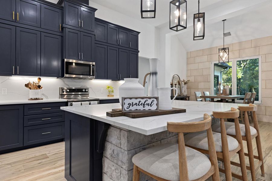 Kitchen with light wood finished floors, light stone countertops, stainless steel appliances, decorative backsplash, and pendant lighting Kitchen with light wood finished floors, light stone countertops, stainless steel appliances, decorative backsplash, and pendant lighting