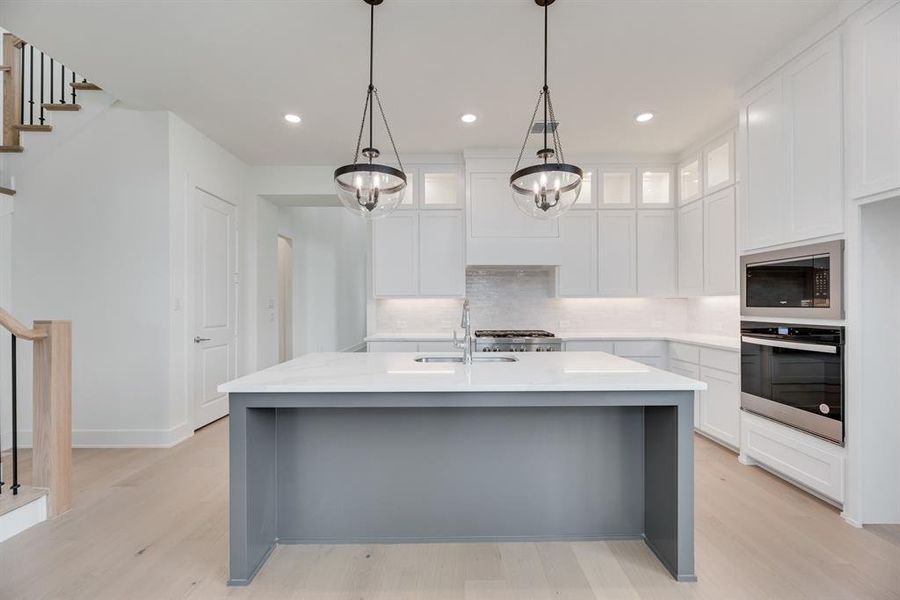 Kitchen with tasteful backsplash, appliances with stainless steel finishes, light wood finished floors, an island with sink, and light stone counters