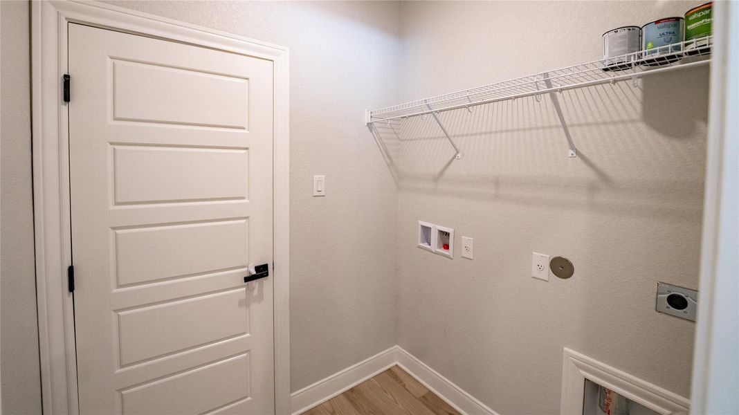 Washroom featuring hookup for a washing machine, light wood-style flooring, electric dryer hookup, and a textured wall Washroom featuring hookup for a washing machine, light wood-style flooring, electric dryer hookup, and a textured wall