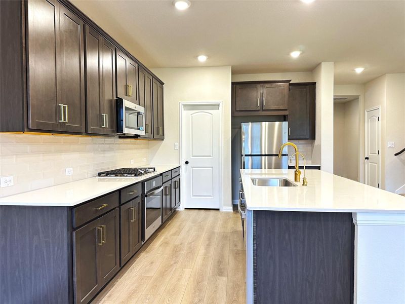 Kitchen with appliances with stainless steel finishes, a sink, a center island with sink, light wood-style flooring, and dark brown cabinetry