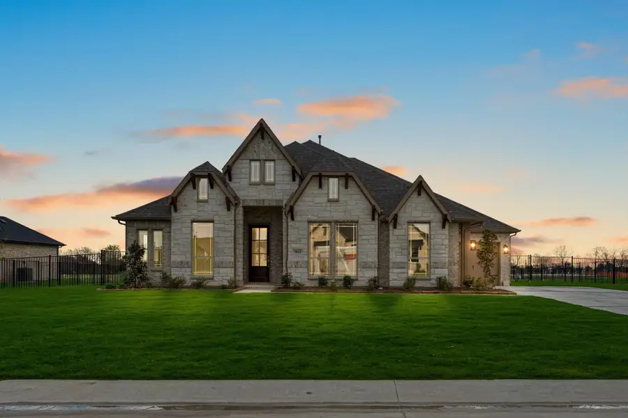 Single-story stone home with dark roof, large windows, and green front lawn at dusk Single-story stone home with dark roof, large windows, and green front lawn at dusk