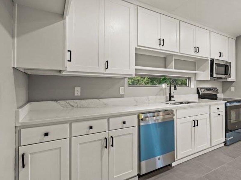 Kitchen with stainless steel appliances, white cabinetry, light stone counters, and open shelves