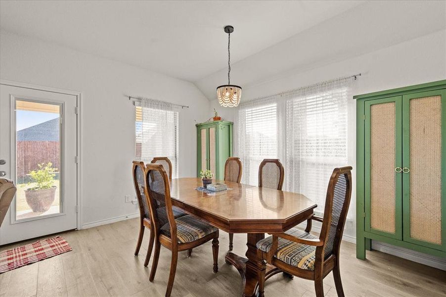 Dining space featuring light hardwood / wood-style floors, lofted ceiling, and an inviting chandelier