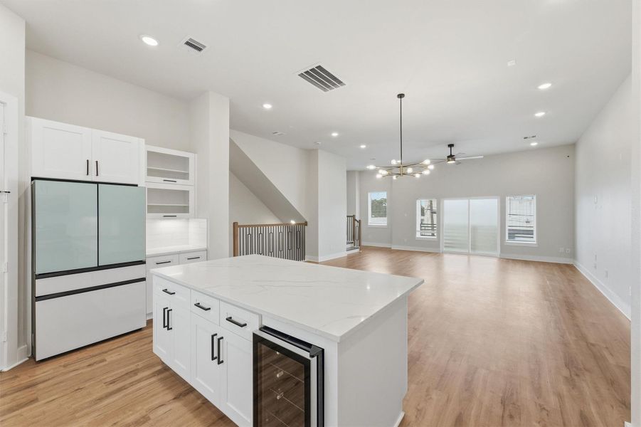 Open-concept kitchen and living area featuring a large quartz island with wine fridge, stainless steel appliances, designer lighting, and seamless flow to a bright, spacious living space.