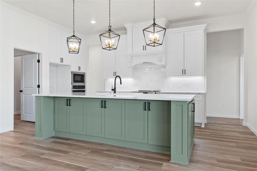 Kitchen featuring green cabinets, white cabinetry, a center island with sink, crown molding, and pendant lighting
