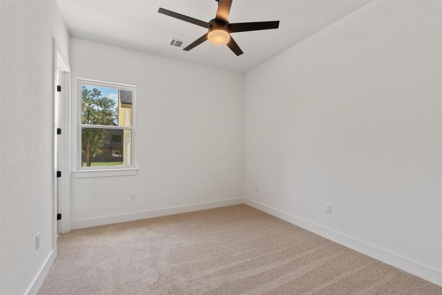 A well-lit bedroom features plush carpeting and a modern ceiling fan for ultimate comfort.