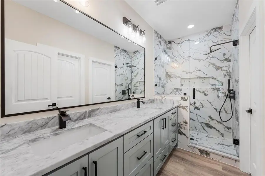 Full bath with a marble finish shower, double vanity, recessed lighting, and wood finished floors