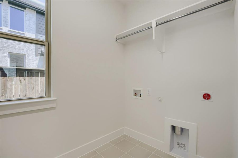 Laundry space featuring light beige tile flooring, a window with a brown frame, and a built-in hanging rod