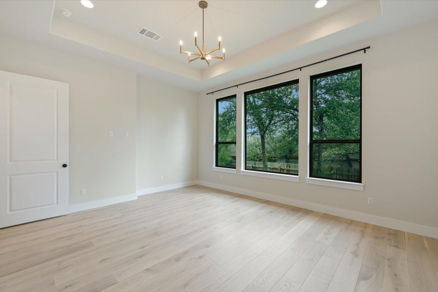 Blonde wood flooring and tray ceilings enhance this spacious living area with abundant natural light.