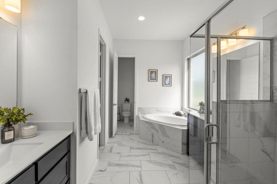Polished tile flooring and a built-in corner tub highlight this elegant primary bathroom.