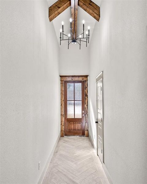 Doorway with beamed ceiling, a textured wall, a high ceiling, and a chandelier